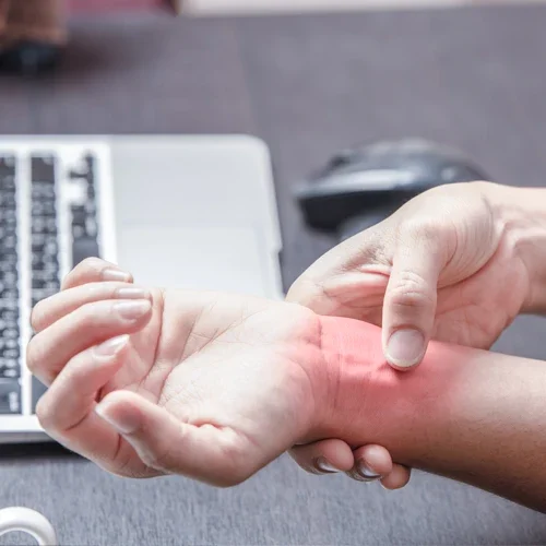 A person pauses their laptop work to grip wrist in pain.